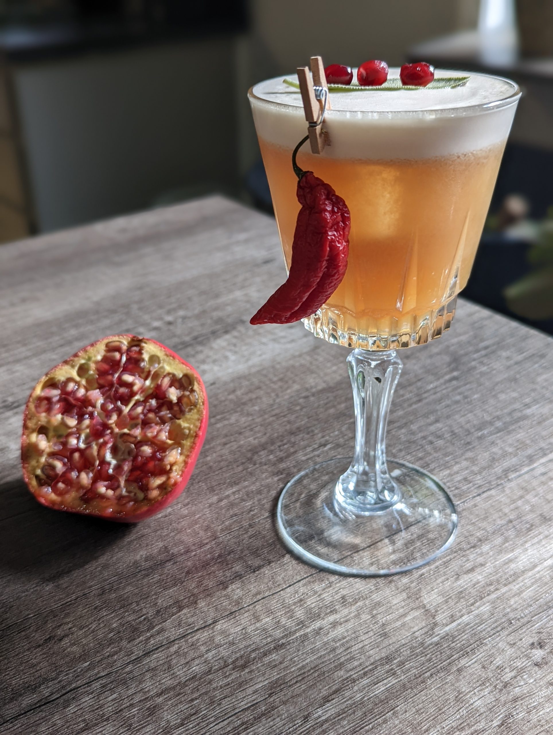 Eggwhite cocktail with a hot pepper garnish and a pomegranate half